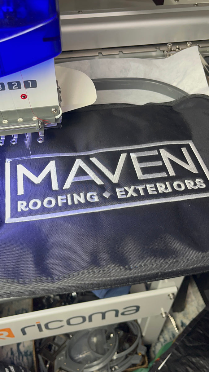 Embroidery machine stitching a company logo onto a navy bag